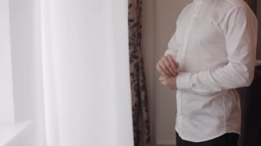 Yakışıklı damat düğün sabahı giyiniyor ve düğmelerini beyaz gömleğin koluna takıyor.