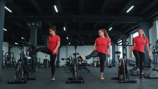 Healthy Caucasian group of women exercising stretching on stationary cycling machine bike in gym — Stock Video