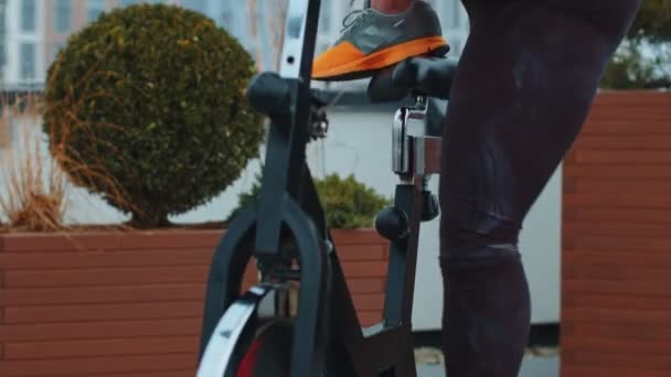 Mujer atlética montando en bicicleta estacionaria de spinning rutina de entrenamiento en la azotea de la casa, pérdida de peso — Vídeos de Stock