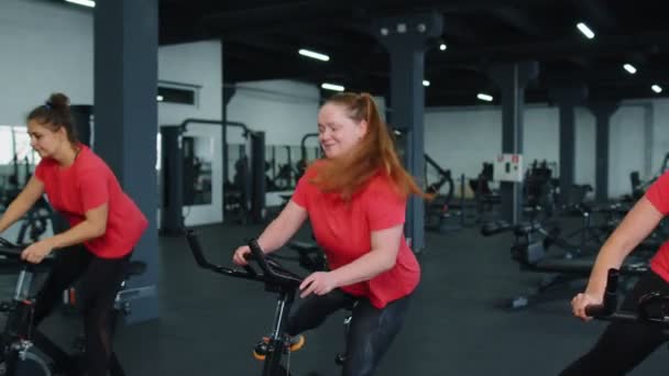 Group athletic girls performing aerobic riding training exercises on cycling stationary bike in gym — Vídeo de Stock