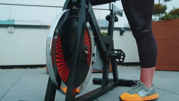 Mujer caucásica saludable haciendo ejercicio en bicicleta de bicicleta estacionaria en el gimnasio de la azotea de la casa — Vídeos de Stock