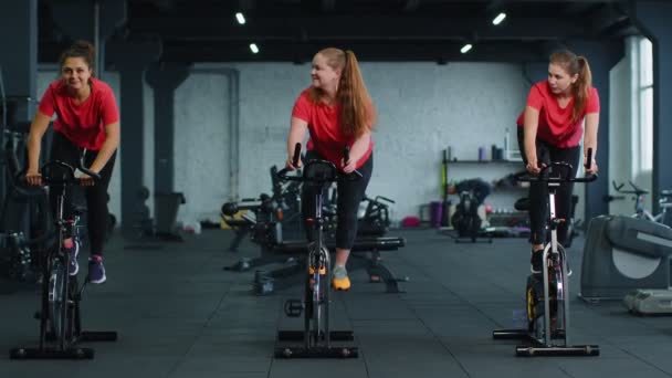 Group athletic girls performing aerobic riding training exercises on cycling stationary bike in gym — Stock Video