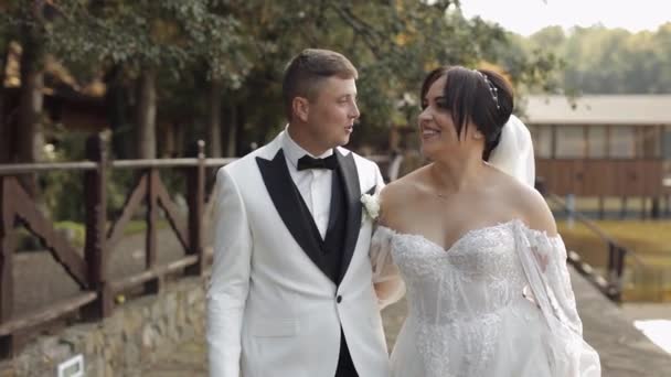 Gyönyörű friss házasok kaukázusi menyasszony vőlegény séta a parkban, kéz a kézben, esküvő pár család — Stock videók