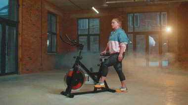 Puslu spor salonunda bisiklet süren atletik bir kadın, kapalı alanda kilo kaybı.