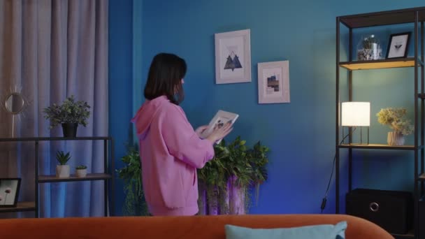 Mujer joven y feliz poniendo la imagen moderna en el marco de la pared azul, la decoración de la sala de estar en el nuevo hogar — Vídeos de Stock