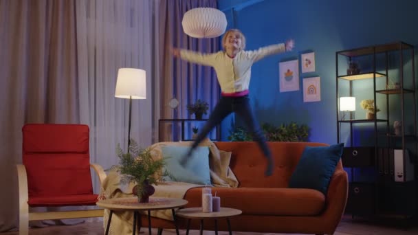 Aktif, komik kız çocuk zıplıyor, dans ediyor, evdeki yumuşak rahat kanepede oynaşıyor yalnız zaman geçiriyor. — Stok video