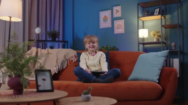 Zmartwiony dzieciak dziewczynka entuzjastycznie gra w gry wideo wyścigowe na telefon komórkowy w domu na kanapie — Wideo stockowe