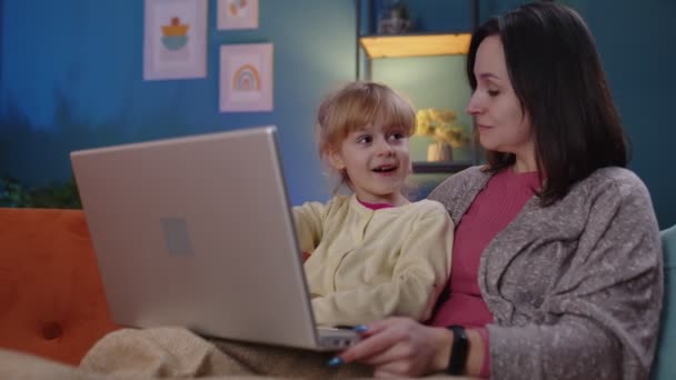 Μητέρα και μικρό παιδί κόρη μελέτη παιδί στο φορητό υπολογιστή, βλέποντας αστείες ταινίες, χαλαρώνοντας, ξαπλωμένος στον καναπέ — Αρχείο Βίντεο