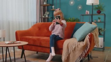 Küçük liseli kız evde kanepede otururken akıllı telefonuyla selfie çekiyor.