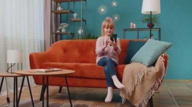 Heyecanlı kazanan kız cep telefonu kullanıyor ve evet diyor evde tek başına sürpriz bir şekilde el kaldırıyor.