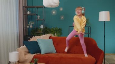 Evde yalnız başına müzik dinlerken kulaklıklı, dans eden ve zıplayan mutlu çocuk.