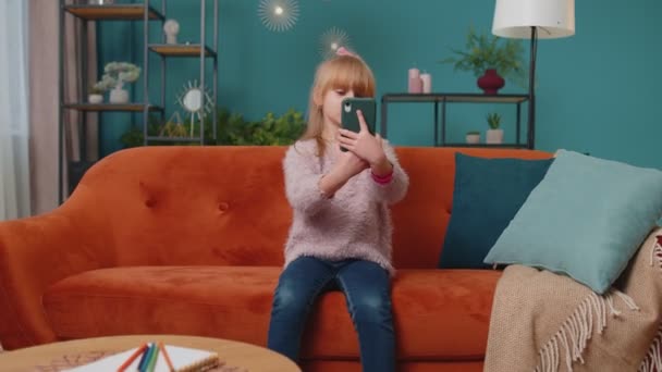 Kleine Schülerin macht Selfie-Foto mit Smartphone, während sie zu Hause auf dem Sofa sitzt — Stockvideo
