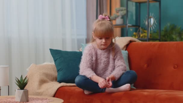 Portrait of little adorable child girl sitting alone on sofa at home looking at camera and smiling — Stock Video