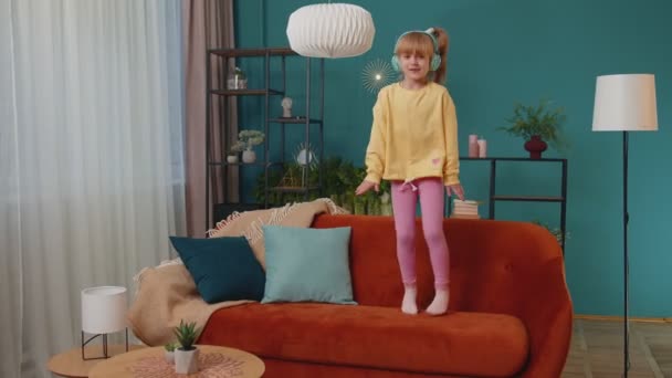 Enfant heureux fille enfant dans les écouteurs danser et sauter tout en écoutant la musique à la maison seul — Video