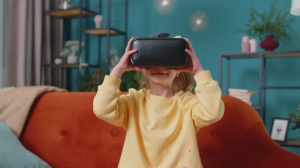 Kleinkind Mädchen sitzt auf dem heimischen Sofa mit Virtual-Reality-Headset Helm-App, um 3D-Videospiel zu spielen — Stockvideo