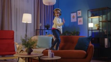 Evde tek başına müzik dinlerken kulaklık takıp dans eden mutlu bir çocuk.