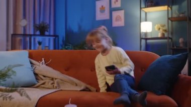 Küçük çocuk akıllı telefonu tutar komik çizgi filmler izler, evde yalnız başına arkadaşlarıyla sohbet eder.