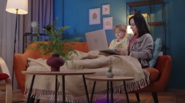 Anne ve küçük çocuk dizüstü bilgisayarda çalışıyor, komik filmler izliyor, dinleniyor, kanepede uzanıyor.