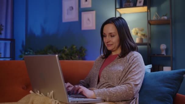 Mujer freelancer acostada en el sofá, trabajando en la pantalla del portátil portátil estudiando compras en línea en casa — Vídeos de Stock