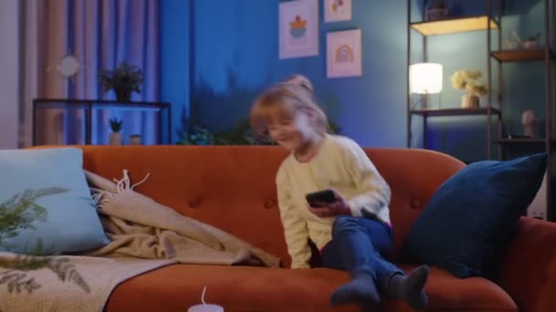 Niño niño sostiene teléfono inteligente viendo dibujos animados divertidos, charlando con amigos en el sofá solo en casa — Vídeo de stock