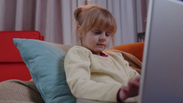 Маленька школярка використовує ноутбук комп'ютерне навчання, читаючи уроки онлайн-освіти наодинці вдома — стокове відео