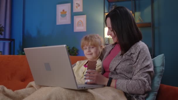 Mor og småbarnsdatter studerer på laptop, ser morsomme filmer, slapper av, ligger på sofa – stockvideo