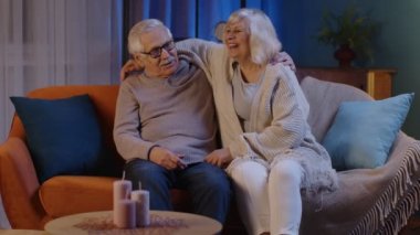 Mutlu yaşlı yaşlı aile çifti modern ev kanepesinde sarılıyor, gülüyor, gülüyor ve konuşuyor.