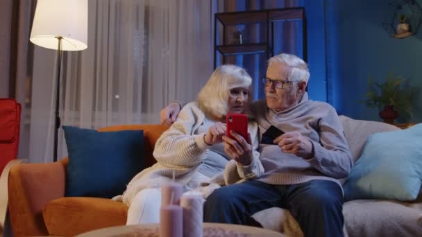 Senior familj par med smartphone hemma, gör online shopping med kreditkort plast bankkort — Stockvideo