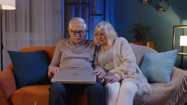 Ευτυχισμένο ηλικιωμένο ζευγάρι που χρησιμοποιεί φορητό υπολογιστή μιλώντας μαζί κάνει online ψώνια στο σπίτι καναπέ — Αρχείο Βίντεο