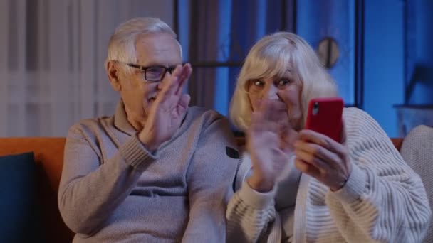 Souriant couple aîné grand-mère grand-père faire un appel vidéo en ligne sur téléphone mobile à la maison canapé — Video