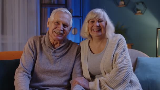 快乐的老人家夫妻抱着，笑着，微笑着看着家里沙发上的相机 — 图库视频影像