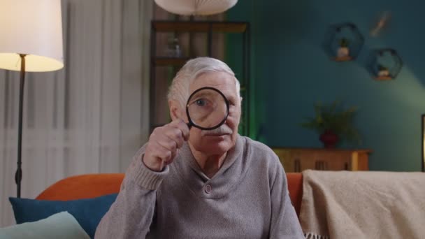 Senior grandfather man looking through magnifying glass, reading, researching, examining at home — Stock Video