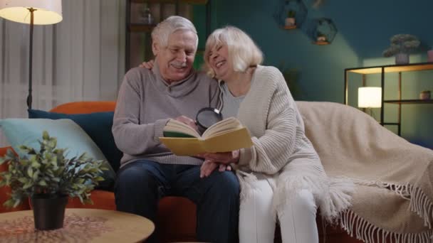 Abuelos mayores pareja relajante, libro de lectura, hablar disfrutando de pasatiempos de ocio en casa de noche — Vídeo de stock