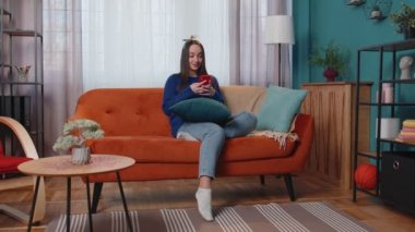 Evde genç bir kadın cep telefonu kullanıyor. Daktilo kullanıyor. 