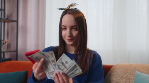 Χαμογελώντας ευτυχισμένη νεαρή γυναίκα κρατώντας μετρητά χρήματα και κινητό τηλέφωνο υπολογίζουν τους εγχώριους λογαριασμούς στο σπίτι — Αρχείο Βίντεο