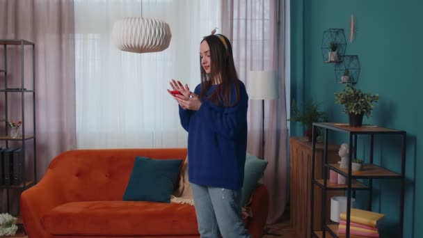Χαρούμενη νεαρή γυναίκα που στέκεται στο σπίτι χρησιμοποιεί το κινητό τηλέφωνο μοιράζεται μηνύματα στην εφαρμογή κοινωνικών μέσων μαζικής ενημέρωσης — Αρχείο Βίντεο