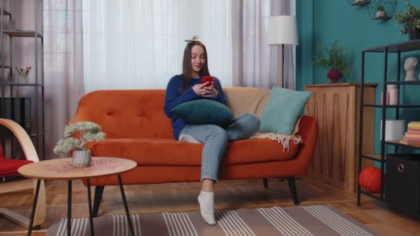 Jonge volwassen vrouw thuis gebruik mobiele telefoon typen browsen zeggen wow ja ontdekte grote overwinning — Stockvideo