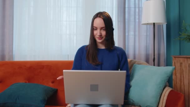 女性のフリーウェアヘッドフォンは、家庭オフィスでラップトップ上で話してビデオ通話指導を行う — ストック動画