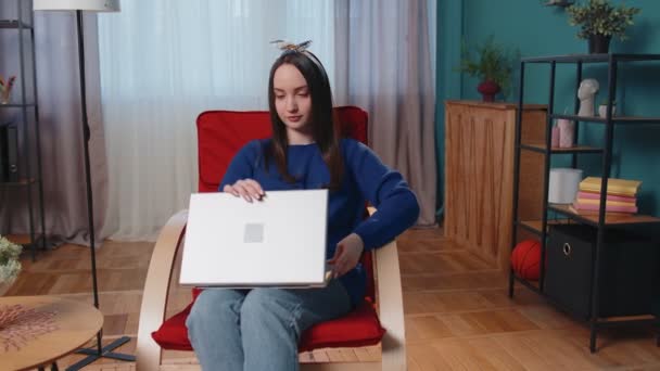 Кавказская молодая женщина, сидящая на диване, открывая ноутбук, начинает работать онлайн в гостиной на дому — стоковое видео