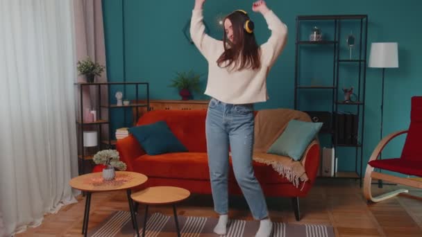 Bella giovane donna caucasica in cuffia ascoltare musica ballare, cantare in soggiorno a casa — Video Stock