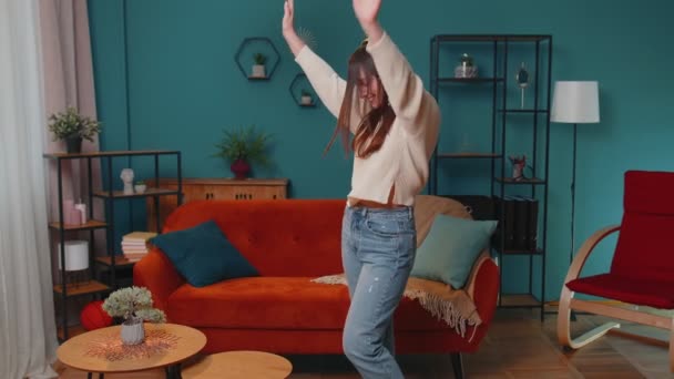Kablosuz kulaklıklı neşeli genç kadın dans ediyor, evdeki oturma odasında rahat bir kanepede şarkı söylüyor. — Stok video