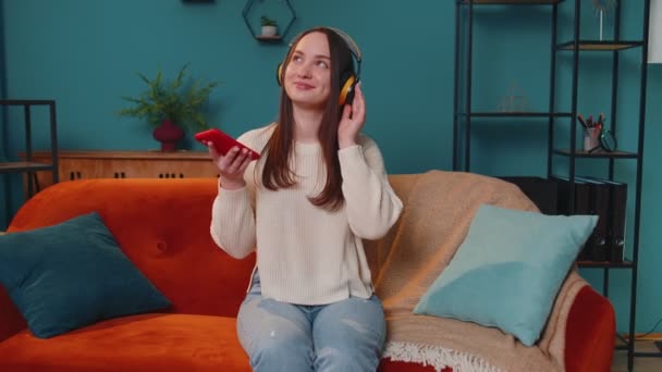 Mujer joven bastante caucásica en auriculares escuchando música bailando, cantando en la sala de estar en casa — Vídeo de stock