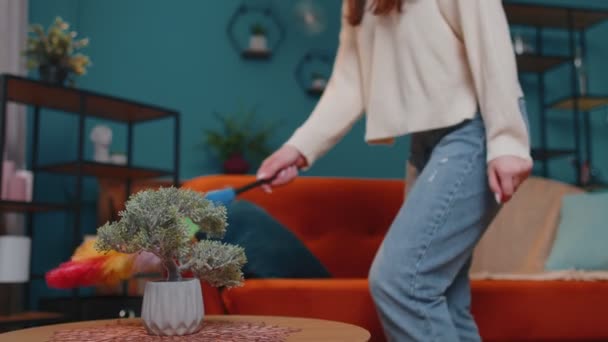Joven mujer bailando desempolvando muebles sola cuidando la higiene usando plumero colorido en la habitación en casa — Vídeos de Stock