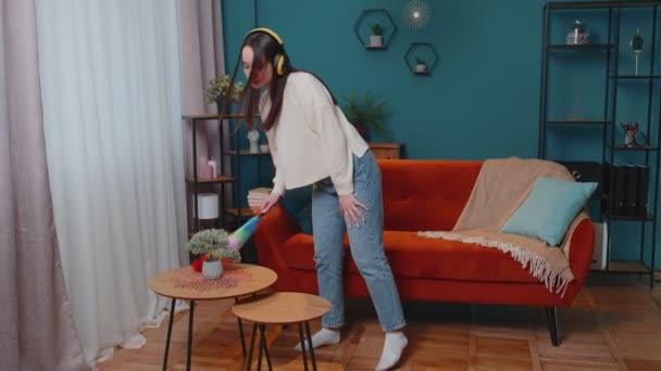 Joven mujer bailando desempolvando muebles sola cuidando la higiene usando plumero colorido en la habitación en casa — Vídeo de stock