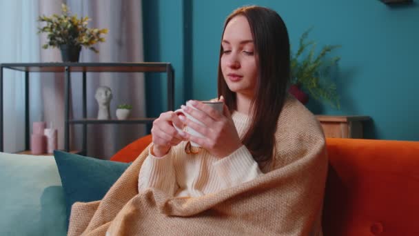 Portretul unei tinere adulte zâmbitoare în pulover alb cald bea o cană de băutură fierbinte relaxându-se acasă — Videoclip de stoc