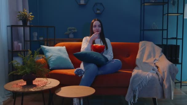 Mujer sentada en el sofá sola, comiendo palomitas de maíz y viendo interesante serie de televisión, película de terror en casa — Vídeos de Stock