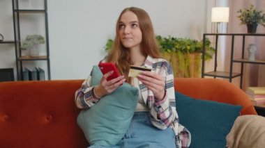 Kadın evde kredi kartı ve akıllı telefon kullanarak para transferi yapıyor.