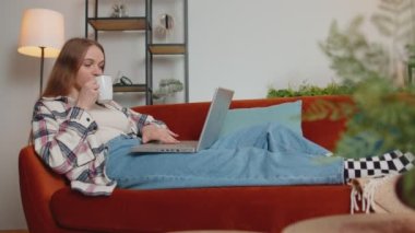 Genç bir kadın evdeki kanepede dizüstü bilgisayar kullanıyor çalışıyor, internetten alışveriş yapıyor.