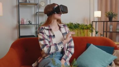 Genç kız evde sanal gerçeklik kulaklığı kullanıyor. 3 boyutlu video oyunu oynuyor. Ellerle jestler yapıyor.