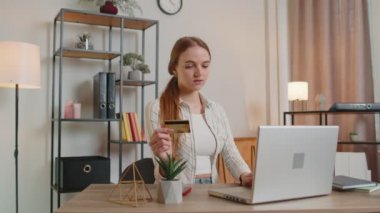 Kadın evde kredi kartı ve dizüstü bilgisayar kullanarak para transfer ederken online alışveriş yapıyor.